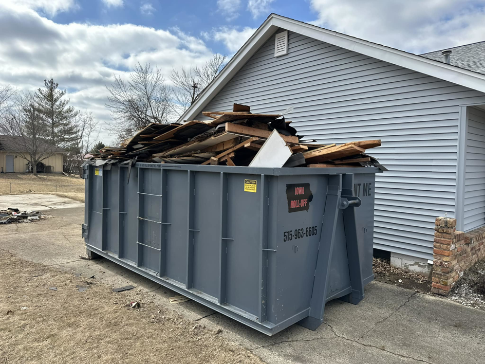 A large roll-off dumpster filled with construction debris next to a house, provided by Iowa Roll Off in Ankeny, IA.