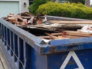 A blue roll-off dumpster filled with wood, cardboard, and other debris for junk removal in Sterling Heights, MI.