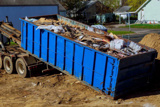 A blue roll-off dumpster filled with construction debris being loaded onto a truck for junk removal in Sterling Heights, MI.