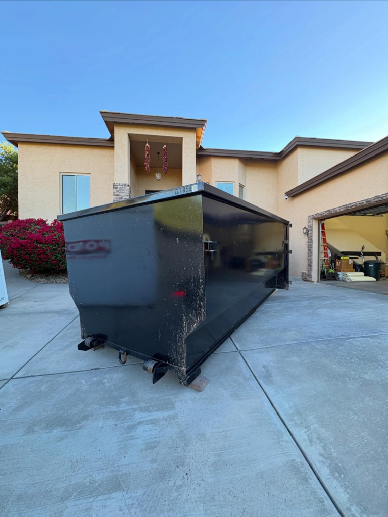 A large black roll-off dumpster placed in a residential driveway for junk removal by Tough Guy Junk Removal in Fountain Hills, AZ.