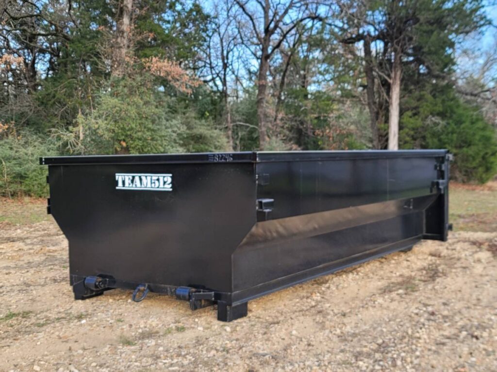 A black roll-off dumpster from Team512 parked in a wooded area, ready for waste removal in Austin, TX