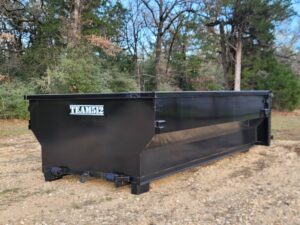 A black roll-off dumpster from Team512 parked in a wooded area, ready for waste removal in Austin, TX