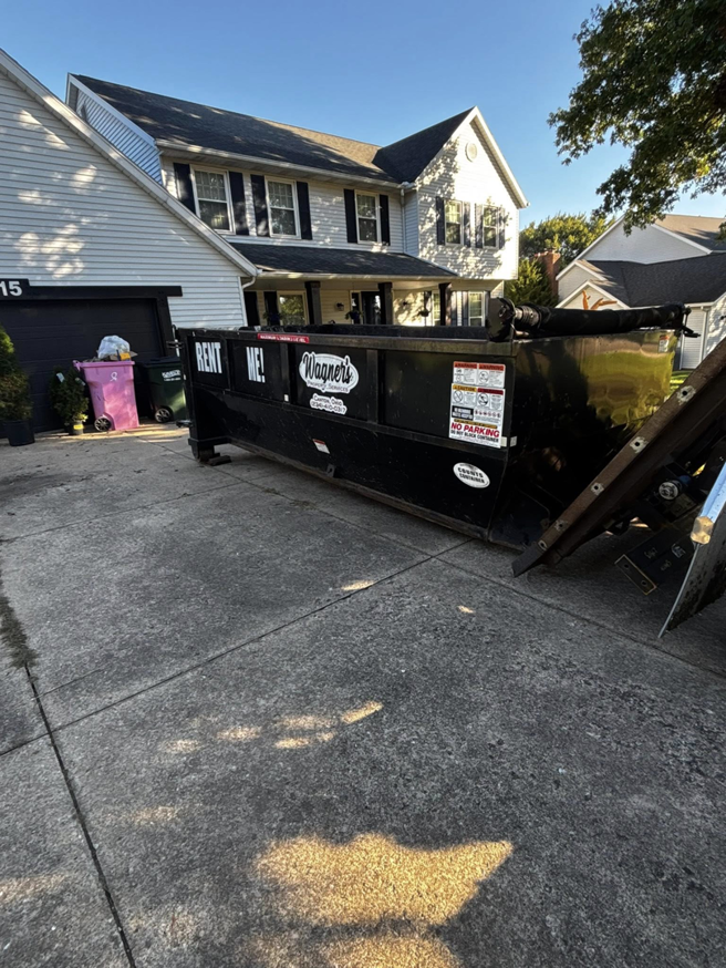 A black roll-off dumpster placed on a residential driveway for junk removal by Wagners Property Services LLC in Canton, OH.