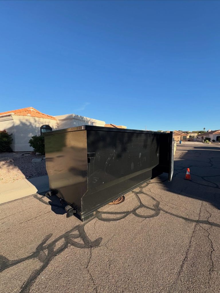 A large black roll-off dumpster placed on a residential street for junk removal by Tough Guy Junk Removal in Fountain Hills, AZ.