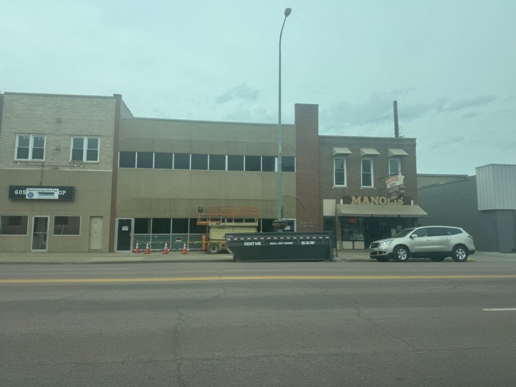 A roll-off dumpster from ClearHouse Hauling placed on a street in Huron, SD, next to a building under renovation.