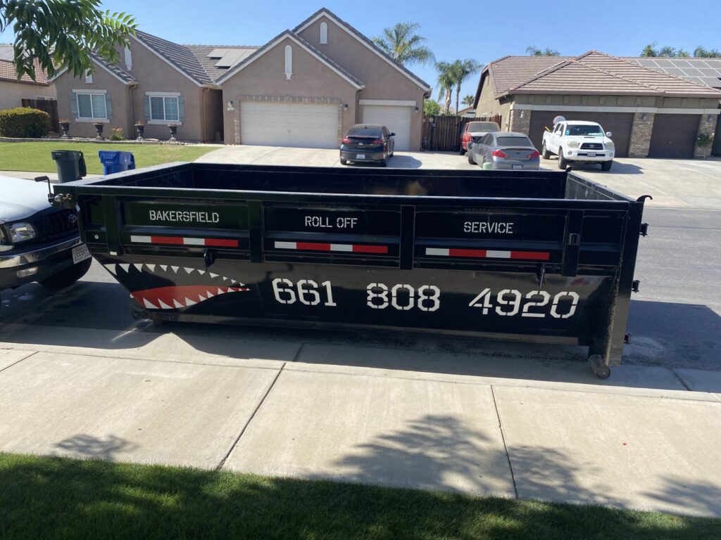 A roll-off dumpster with the business name delivered to a residential driveway by Bakersfield Roll-Off Service in Bakersfield, CA.