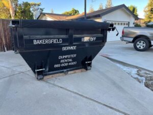 A roll-off dumpster with the business name placed in a residential driveway for junk removal by Bakersfield Roll-Off Service in Bakersfield, CA.
