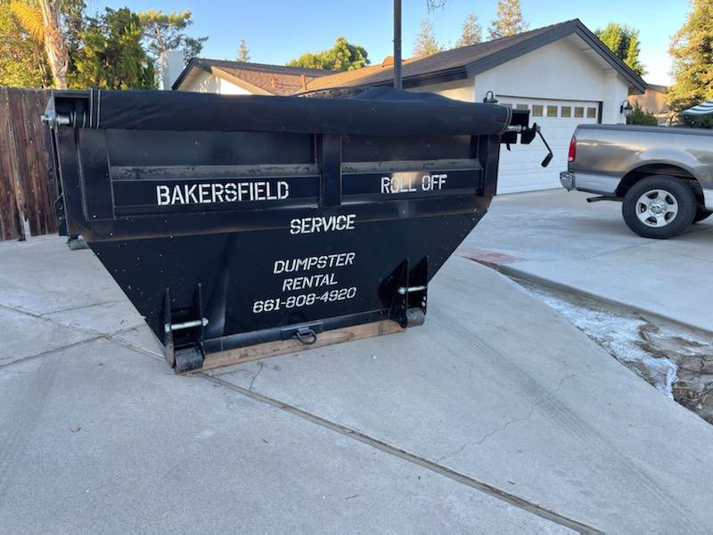 A roll-off dumpster with the business name placed in a residential driveway for junk removal by Bakersfield Roll-Off Service in Bakersfield, CA.