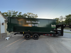 A green roll-off dumpster trailer from MoJo Hauling LLC delivered to a residential driveway in Bartlesville, OK.