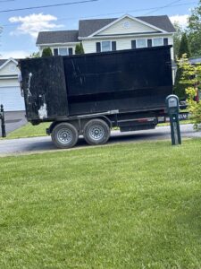 A large black roll-off dumpster on a trailer parked in front of a residential home by Dumpin' Junk in Martinsburg, WV.