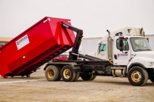 A Bosman Waste Services truck deploying a red roll-off dumpster for junk removal in Roanoke, TX.