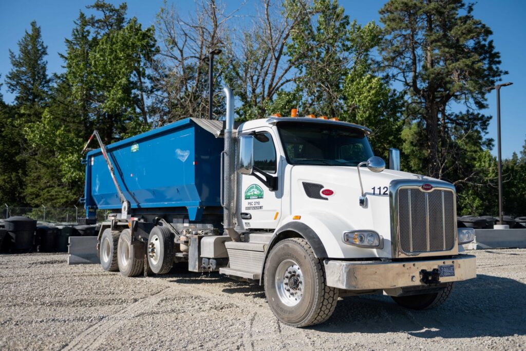 A white roll-off dumpster truck with a blue container for junk removal services by Evergreen Disposal in Kalispell, MT.