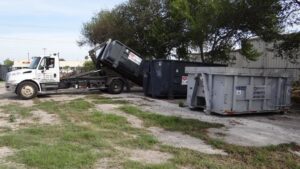 A roll-off dumpster truck from White Star Services LLC loading a dumpster on a job site in Corpus Christi, TX.