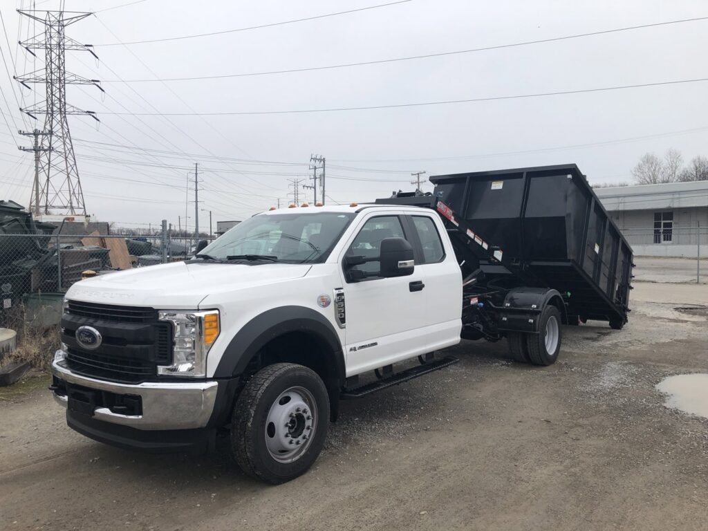 A white Ford truck equipped with a black roll-off dumpster for junk removal services by Music City Removal in Nashville, TN.