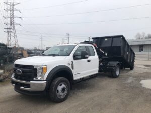 A white Ford truck equipped with a black roll-off dumpster for junk removal services by Music City Removal in Nashville, TN.
