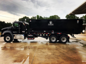 A black roll-off dumpster truck from Warrior Waste Services parked on a wet surface in Northport, AL.
