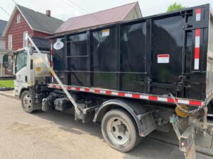 A white roll-off dumpster truck from Wint Services, LLC, with a black container parked on a residential street in Colorado Springs, CO.