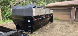 A large black roll-off dumpster with a protective tarp, ready for junk removal services by At Ease Dumpsters and Junk Removal in Welch, MN.