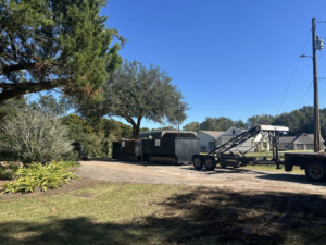 Multiple roll-off dumpsters being delivered or picked up by a truck and trailer for Local Dumpster Rentals LLC in Breaux Bridge, LA.