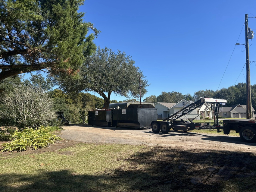 Multiple roll-off dumpsters being delivered or picked up by a truck and trailer for Local Dumpster Rentals LLC in Breaux Bridge, LA.