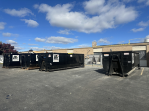 Several black roll-off dumpsters from Logistics Recycling Inc. parked in a lot in Green Bay, WI, ready for junk removal.