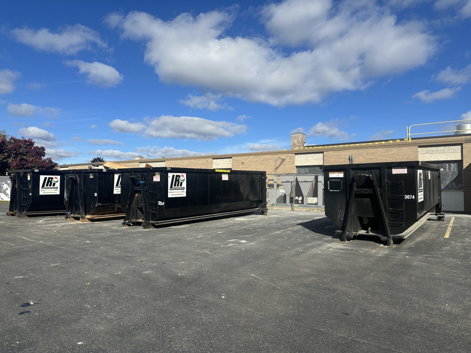 Several black roll-off dumpsters from Logistics Recycling Inc. parked in a lot in Green Bay, WI, ready for junk removal.