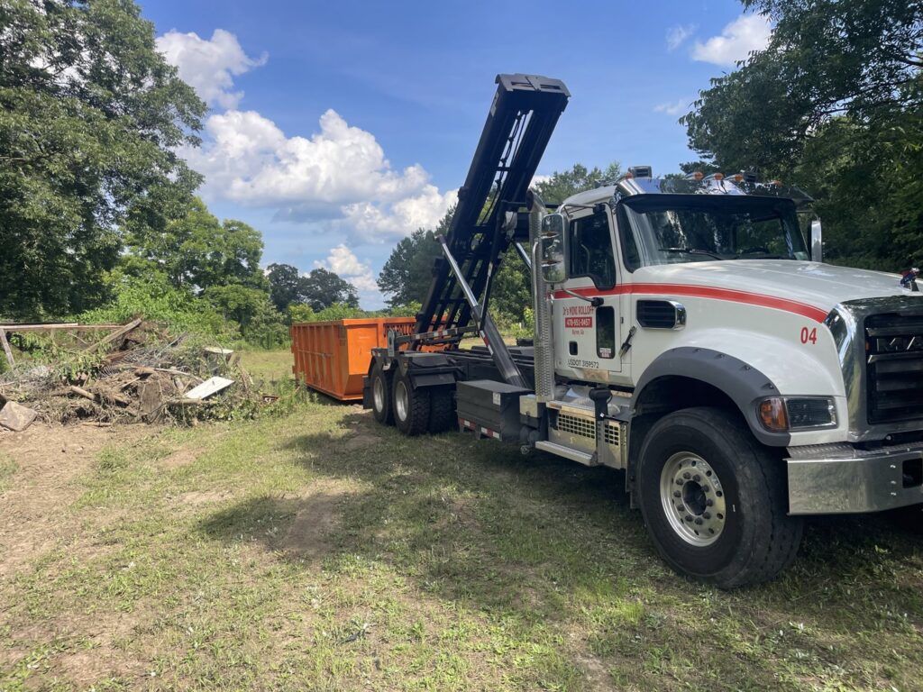 A Jr's Mini Roll Off LLC truck with a roll-off dumpster near a pile of brush for removal in Byron, GA.