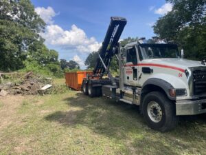 A Jr's Mini Roll Off LLC truck with a roll-off dumpster near a pile of brush for removal in Byron, GA.