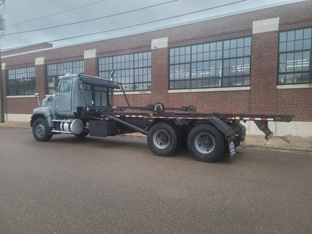 A grey roll-off truck, part of the Community Disposal fleet, used for transporting dumpsters in Jacksonville, FL.