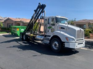 A roll-off truck from Junk Control delivering a green dumpster on a residential street in Henderson, NV.