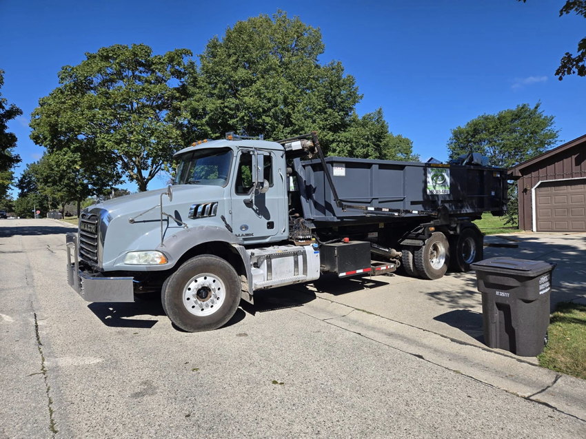 A roll-off truck delivering a dumpster on a residential street for Premier Recycling and Disposal in Waukesha, WI.