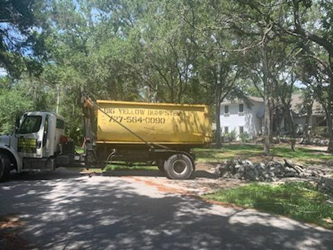 A roll-off truck with a Big Yellow Dumpster next to a pile of demolition debris on a residential street in Saint Petersburg, FL.
