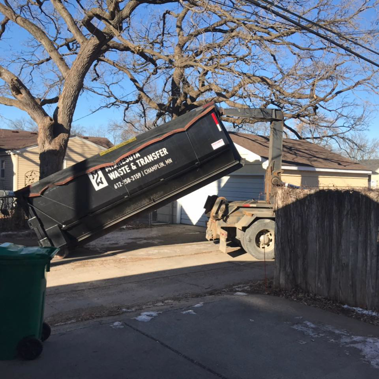A roll-off truck from Minnesota Waste and Transfer deploying a large dumpster in a residential driveway in Champlin, MN