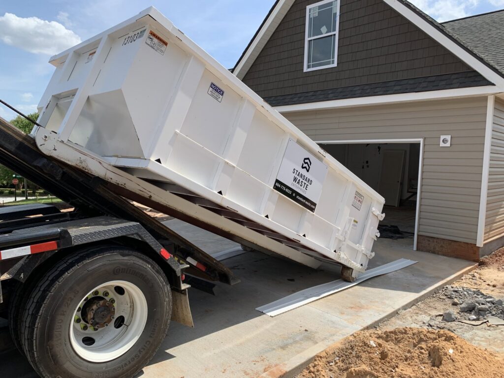 A roll-off truck deploying a large white dumpster at a residential construction site, provided by Standard Waste Enterprises in Greenville, SC.