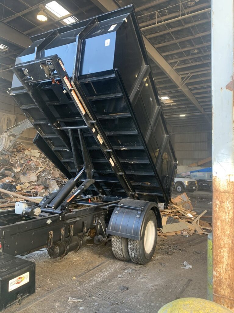 A roll-off truck from Convenient Disposal & Sanitation dumping construction debris at a waste transfer station in Fall River, MA.