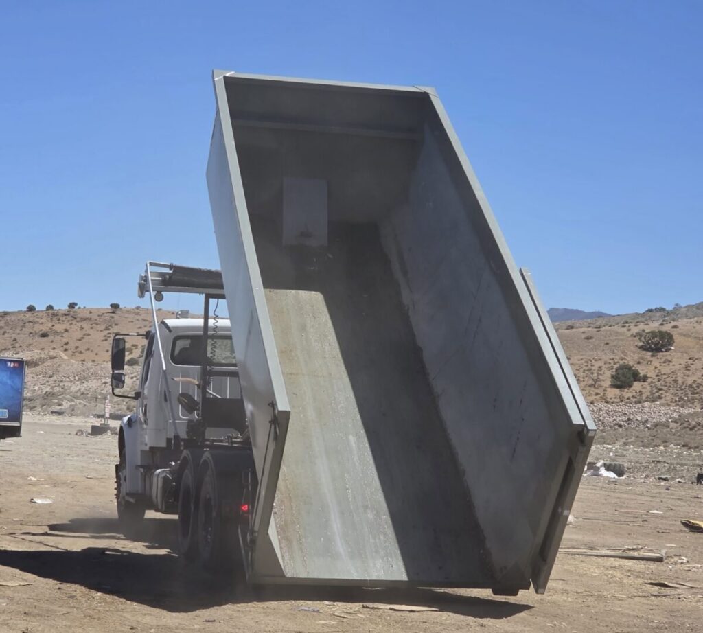 A Trash Panda roll-off truck dumping an empty dumpster, demonstrating waste management services in Carson City, NV.