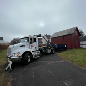 A Chet's Disposal roll-off truck with a dumpster parked near a red barn in Springfield, MA.