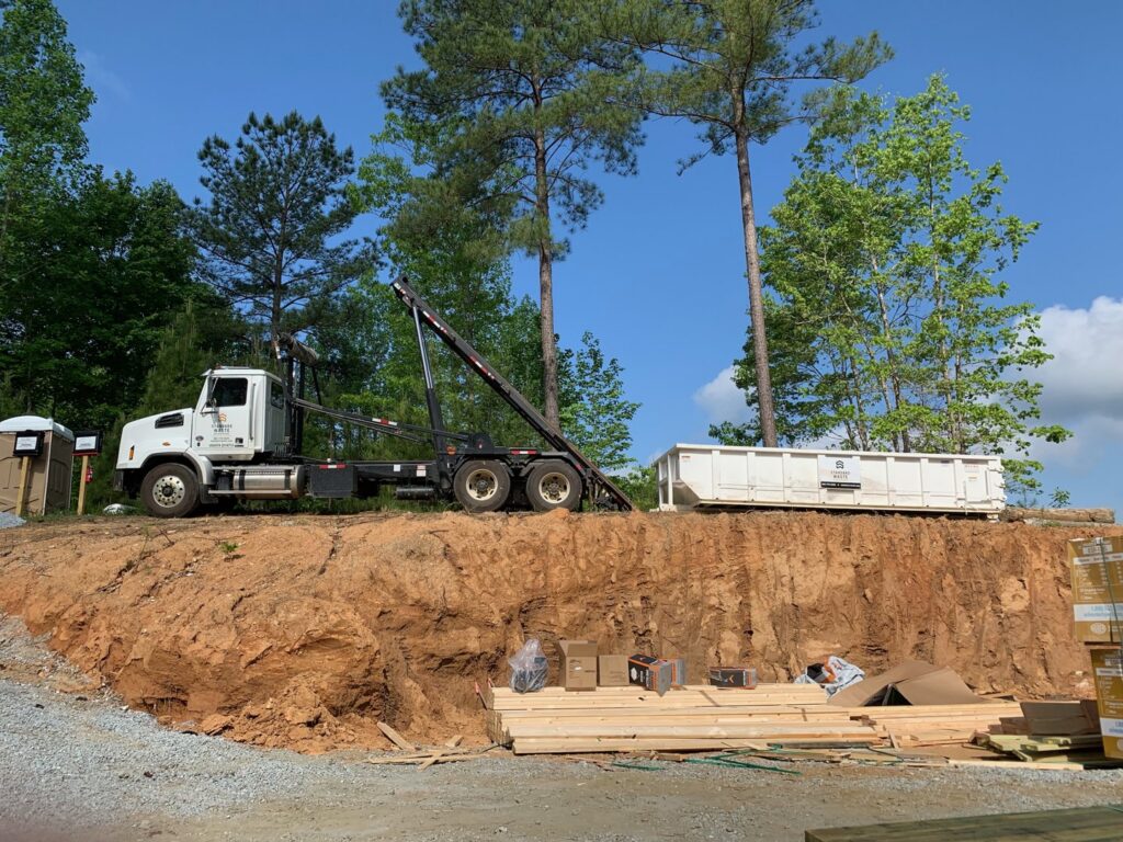 A roll-off truck with a white dumpster placed on a dirt mound at a construction site, demonstrating services by Standard Waste Enterprises in Greenville, SC.