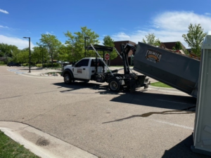 A Premier Roll Off Services truck actively delivering or picking up a dumpster in a parking lot in Thornton, CO.