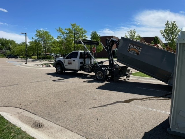 A Premier Roll Off Services truck actively delivering or picking up a dumpster in a parking lot in Thornton, CO.