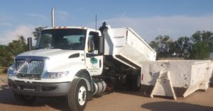 A white roll-off truck deploying a large dumpster for junk removal services by EM Enterprises, Inc. in Cheyenne, WY.