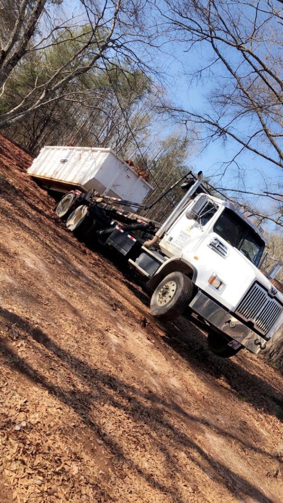 A roll-off truck with a dumpster on a dirt road, providing junk removal services for Standard Waste Enterprises in Greenville, SC.