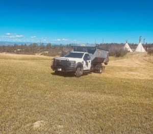 A Premier Roll Off Services truck with a dumpster parked in a sunny grassy field in Thornton, CO, for junk removal.