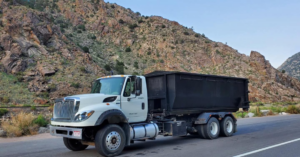 A white roll-off truck with a black dumpster container on a mountain road for Arkansas Valley Roll-Off in Salida, CO.