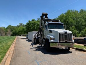A roll-off truck with a white dumpster on a paved road, providing junk removal services for Standard Waste Enterprises in Greenville, SC.