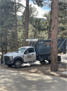 A Premier Roll Off Services truck with a dumpster parked among pine trees, ready for junk removal in Thornton, CO.