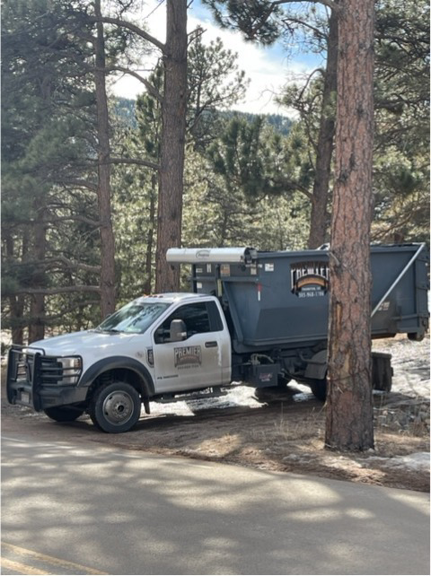 A Premier Roll Off Services truck with a dumpster parked among pine trees, ready for junk removal in Thornton, CO.