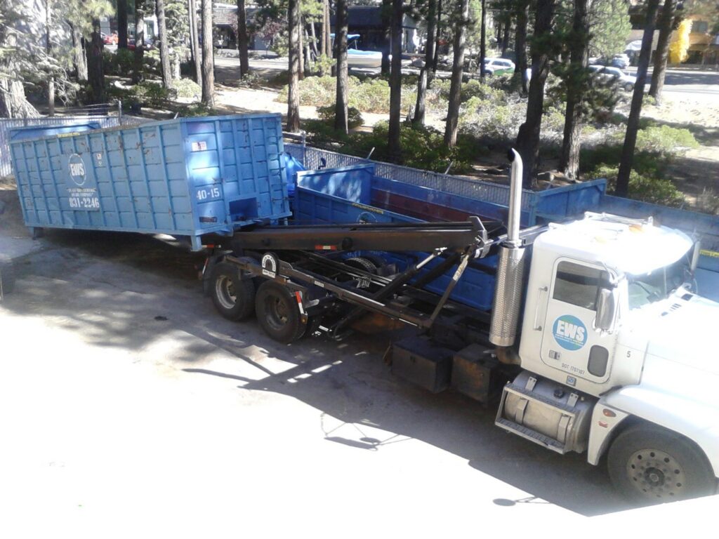 A roll-off truck from Empire Waste Systems in Carson City, NV, loading a blue dumpster for junk removal