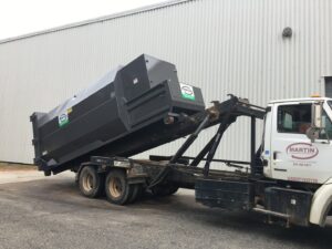 A Martin Environmental roll-off truck loading a large dumpster in Dothan, AL.