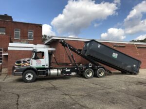 A Martin Environmental roll-off truck lowering a large dumpster in front of a brick building in Dothan, AL.
